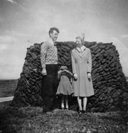 Perfectionists took pride in building their peats, and stacks were often a backdrop for a photo, like for Norman, Iris, and Sandra MacKenzie in their Sunday best at Sheshader, Lewis.